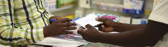 A pharmacy staff member handing a customer their medication at the counter